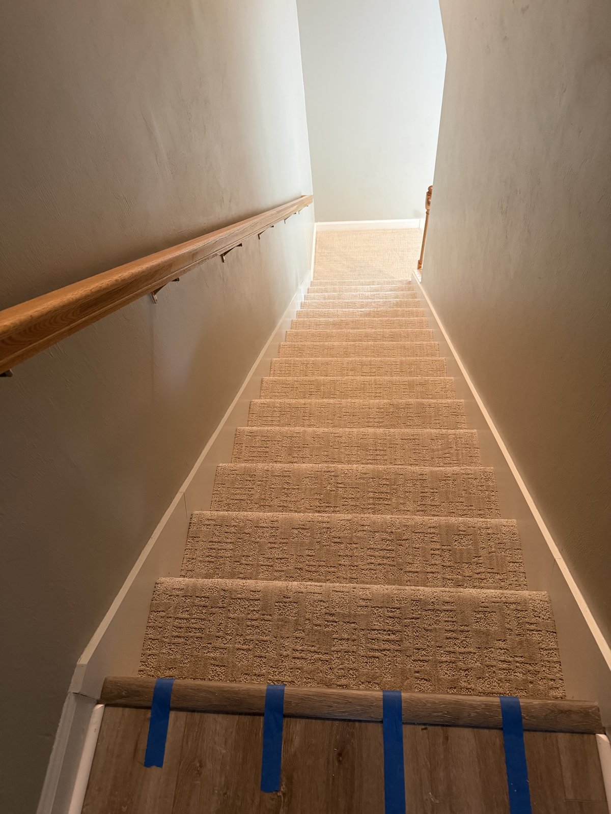 Carpeted staircase descending a hallway with oak handrail